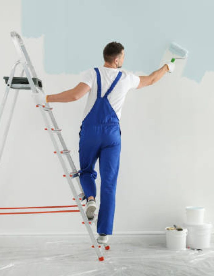 Man painting wall with light blue dye indoors, back view