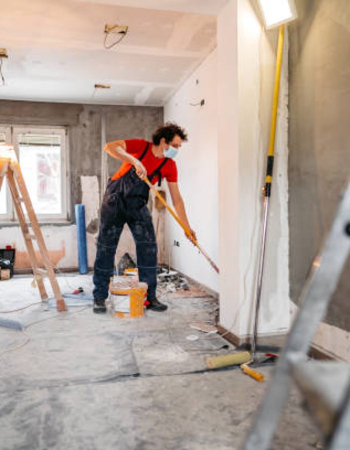 Young man painting apartment walls and renovating apartment. He is wearing protective face mask.